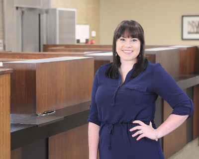 Picture of employee, Carlie Tawzer, wearing a navy dress and standing in the Omega Branch Lobby.
